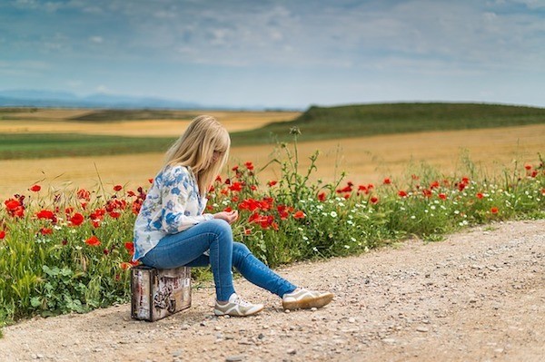 Woman waiting by field with suitcase