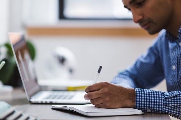 man with pen and pad at computer